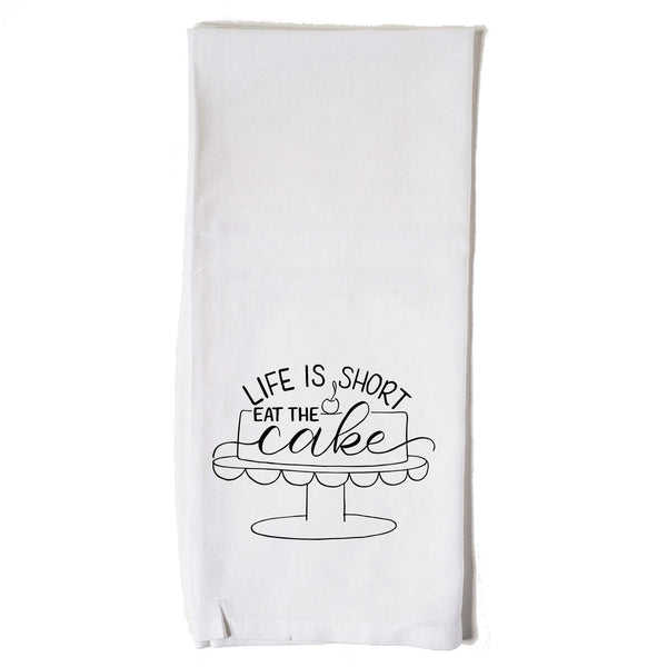 White floursack towel with black hand lettered illustrated design that says Life is short eat the cake with a cake on a stand doodle