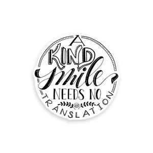 3" hand lettered illustrated vinyl sticker saying a kind smile needs no translation in black and white