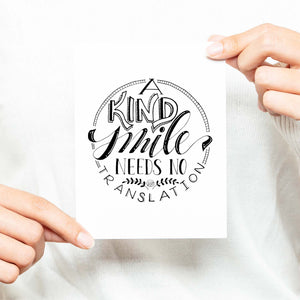 A Kind Smile Needs No Translation A2 Greeting Card black design on white card with white envelope shown with a woman in a white sweater holding card