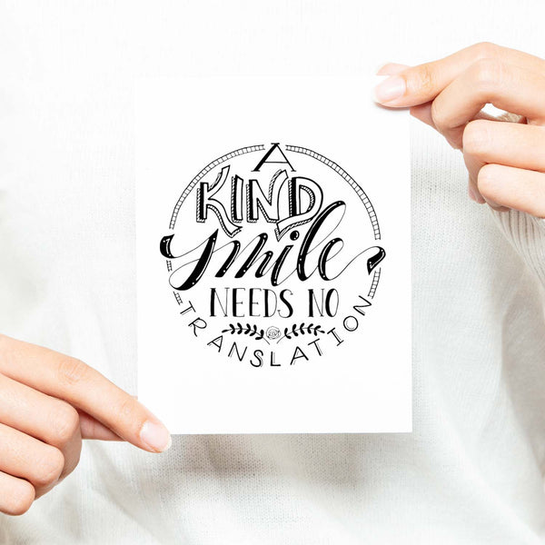 A Kind Smile Needs No Translation A2 Greeting Card black design on white card with white envelope shown with a woman in a white sweater holding card