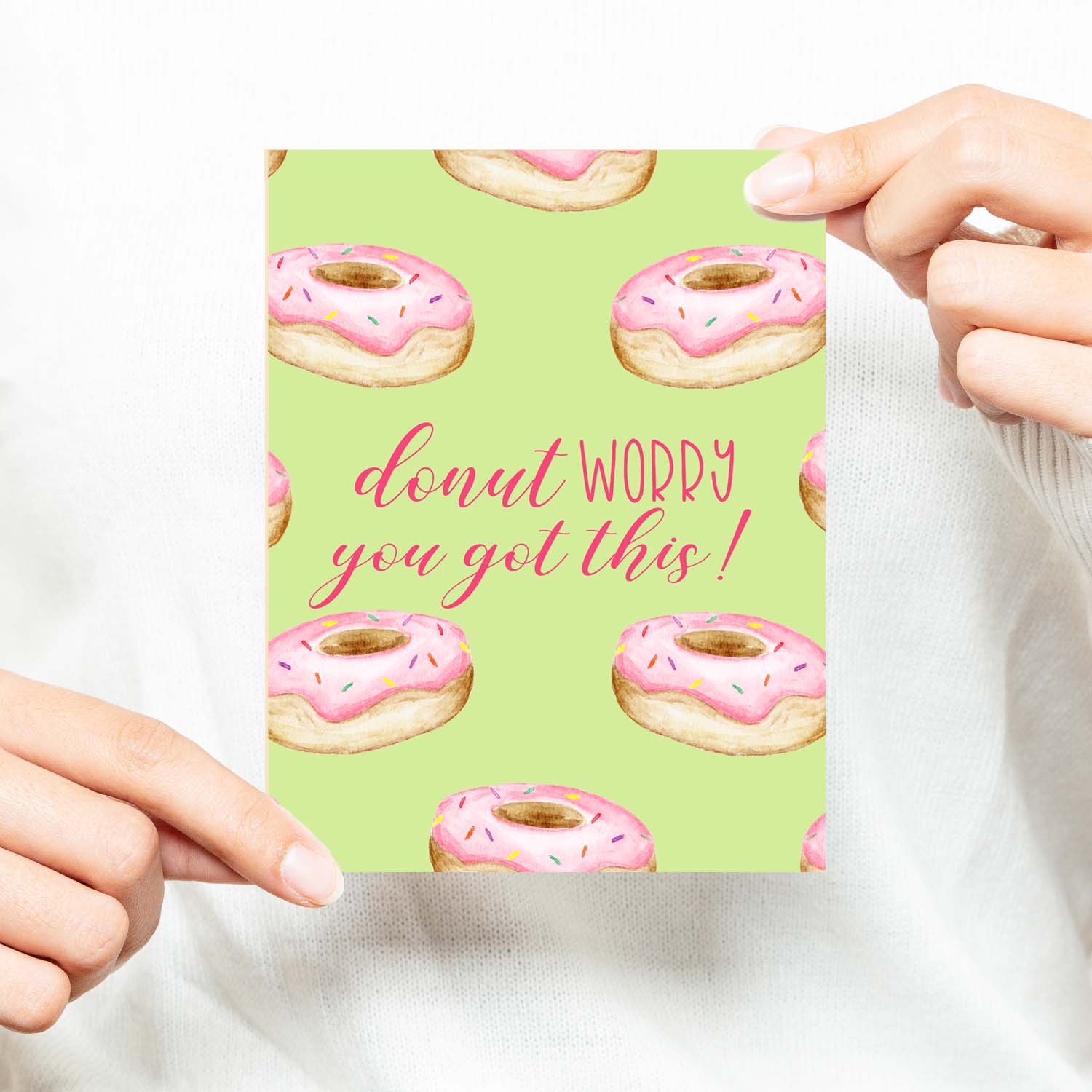 watercolor pink frosted donuts with sprinkles on a greeting card that says donut worry you got this with a white A2 envelope shown with a woman in a white sweater holding card