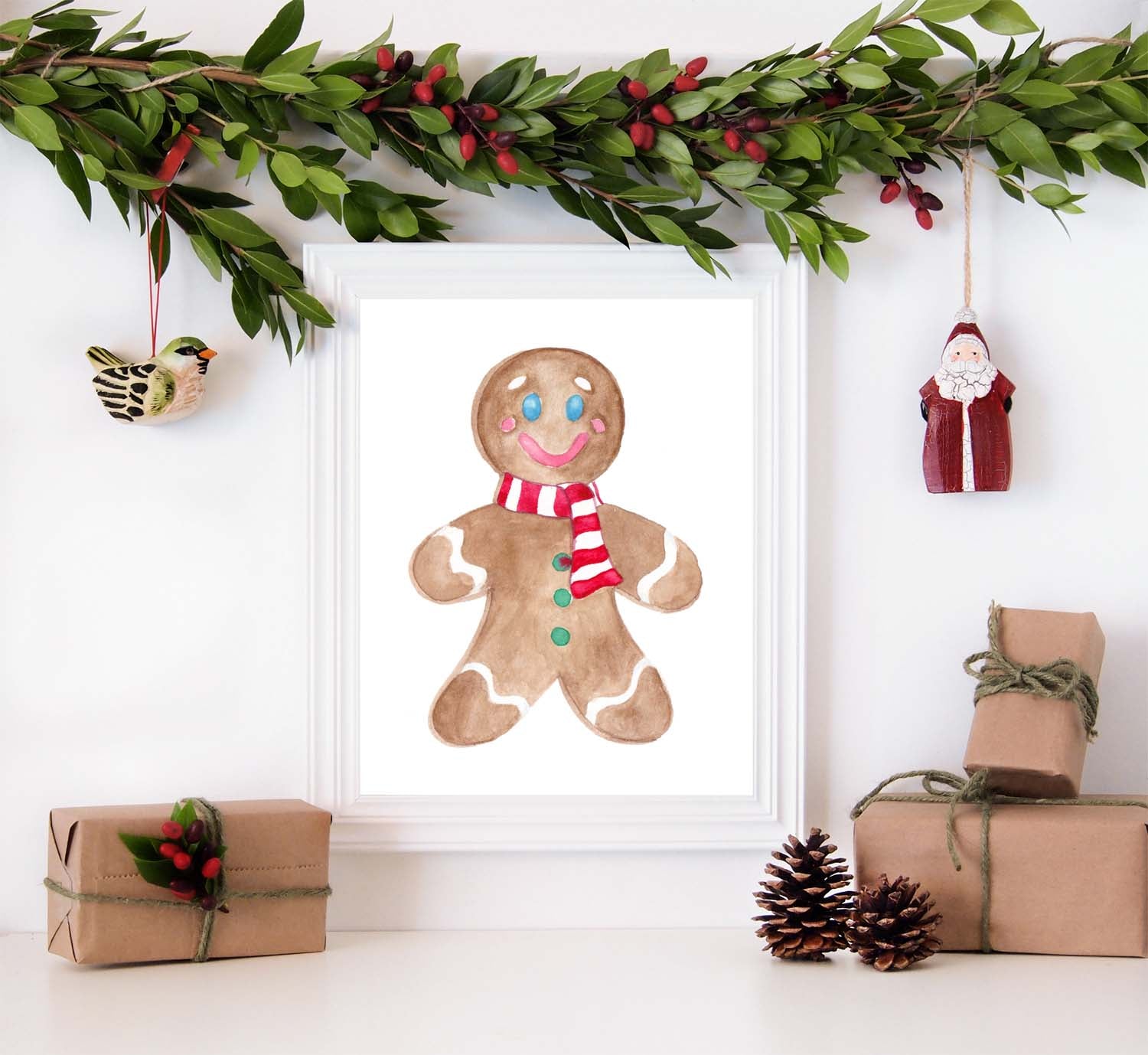 Watercolor gingerbread man painting with a red and white striped scarf shown in a white frame surrounded by christmas decorations