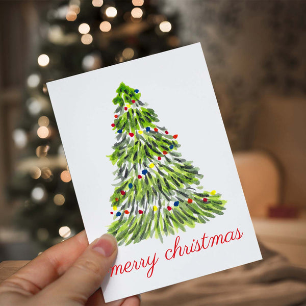 Merry Christmas greeting card with a watercolor Christmas tree with colorful lights and merry christmas message  shown with a woman holding in front of a lighted christmas tree