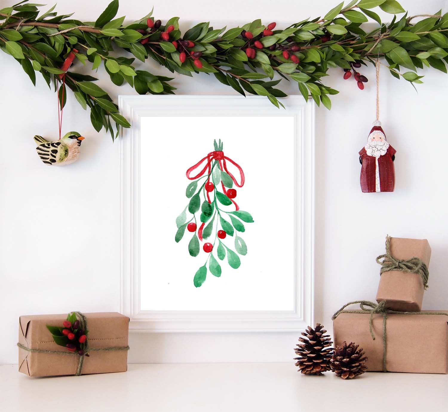 Watercolor painting of mistletoe tied with a red ribbon in a white frame and surrounded by christmas decorations