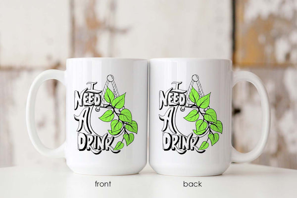 15oz white ceramic mug with hand lettered illustrated design that says I need a drink with an illustration of a pothos plant with green leaves in a hanging pot showing both the front and the back of the mug