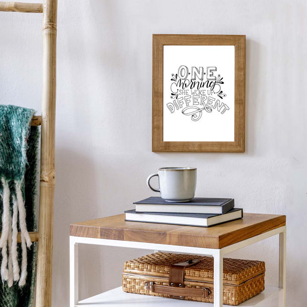 Original black and white illustrated wall art that says one morning she woke up different shown hanging on a bedroom wall near a stack of books and a mug