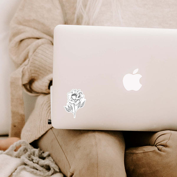 3" hand illustrated, black and white botanical peony vinyl sticker shown adhered to a MacBook laptop cover sitting open on a woman's lap