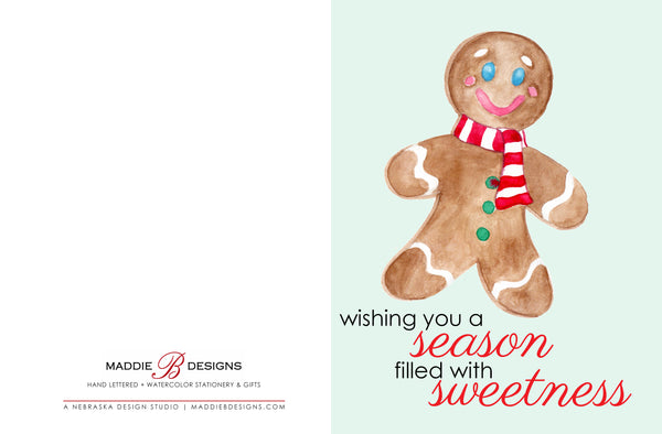 Watercolor Christmas card with a happy watercolor gingerbread man that says wishing you a season filled with sweetness laying flat showing front and back of card