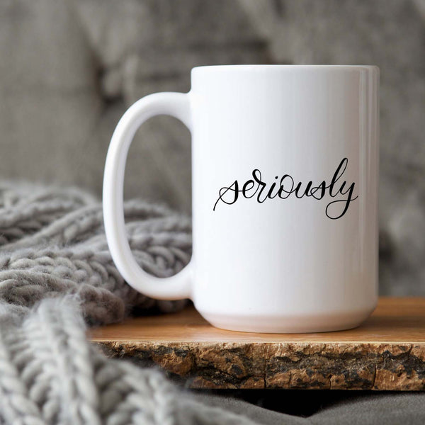 15oz white ceramic mug with hand lettered illustrated design that says seriously shown sitting on a wood tray with a grey knit blanket