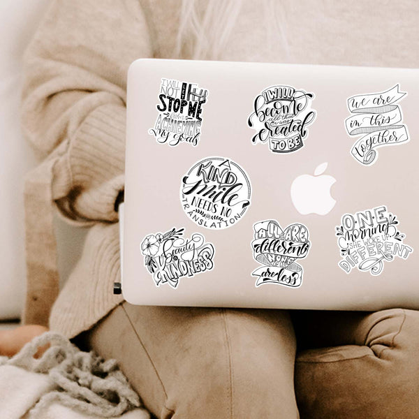 Collection of inspirational and motivational black and white stickers shown on a MacBook cover sitting open on a woman's lap