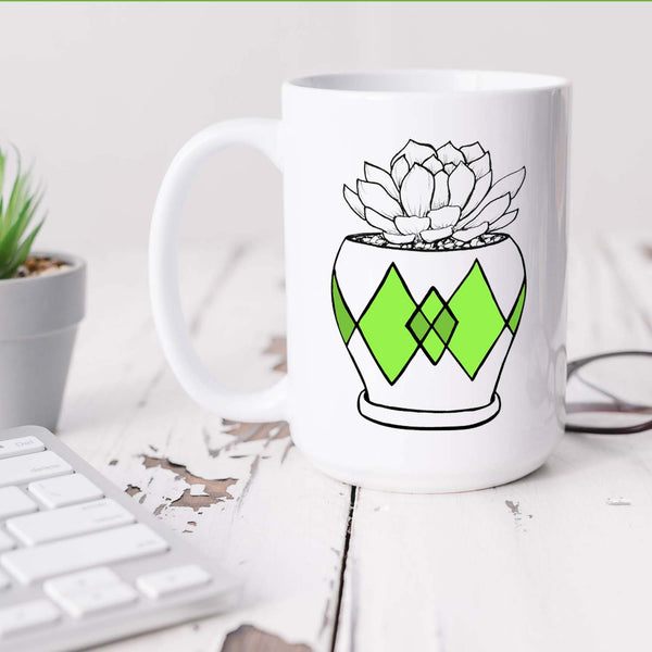 15oz white ceramic mug with hand lettered illustrated design of a succulent plant in a pot with green diamond pattern shown sitting on a white office desk